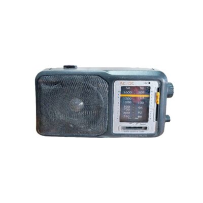 radio portátil de época de diseño clásico, caracterizada por su carcasa rectangular en tonos oscuros, un altavoz lateral protegido por una rejilla metálica circular y un panel de sintonía analógico frontal con diales para bandas AM y FM y controles laterales alquiler para eventos, publicidad, peliculas y series