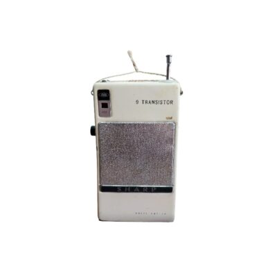 radio portátil de época de la marca Sharp, caracterizada por su carcasa rectangular vertical de tonos claros, una antena telescópica superior, una inscripción superior con la leyenda "9 Transistor" y una rejilla metálica frontal texturizada en la sección central alquiler para eventos, publicidad, peliculas y series