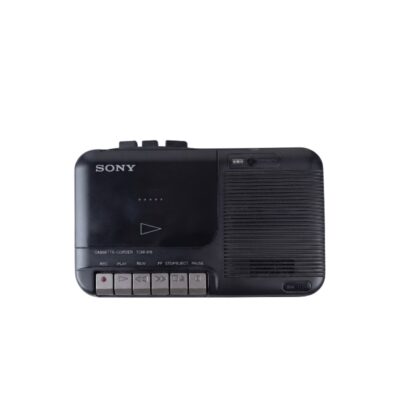 reproductor de casete portátil de época de la marca Sony (modelo Cassette-Corder TCM-818), caracterizada por su carcasa rectangular compacta en tonos oscuros, un compartimento superior para la cinta y un banco de teclas de control mecánico frontal para la gestión de grabación, reproducción y avance alquiler para eventos, publicidad, peliculas y series