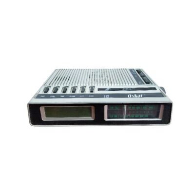 radio despertador de sobremesa de época de la marca Oskar, caracterizada por su carcasa rectangular compacta de perfil bajo en tonos claros, una hilera superior de múltiples botones mecánicos de control y ajuste, y un panel frontal que combina una pantalla digital con un dial de sintonización analógico alquiler para eventos, publicidad, peliculas y series