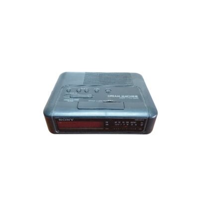 radio despertador de época de la marca Sony (modelo Dream Machine), caracterizada por su carcasa rectangular compacta y redondeada en tonos oscuros, un panel superior con controles e interruptores integrados y una pantalla digital frontal combinada con un sintonizador de radio AM/FM alquiler para eventos, publicidad, peliculas y series