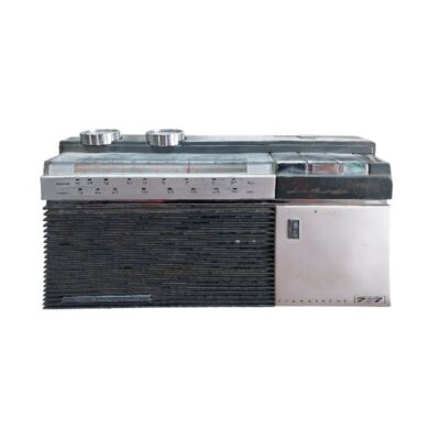 radio transistor portátil de época, caracterizada por su carcasa rectangular con mandos de control superiores, un panel de sintonía analógico horizontal y un diseño frontal combinado que incluye una amplia rejilla de altavoz de lamas horizontales oscuras junto con una sección metálica lateral plateada que incorpora la inscripción del modelo 767 alquiler para eventos, publicidad, peliculas y series