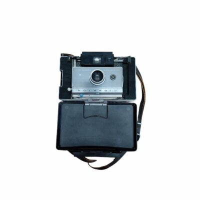 cámara fotográfica instantánea clásica de fuelle de la reconocida marca Polaroid, modelo Automatic 104 Land Camera, que se muestra abierta con su cuerpo metálico y plástico, lente central y tapa abatible inferior junto con su correa de transporte alquiler para eventos, publicidad, peliculas y series