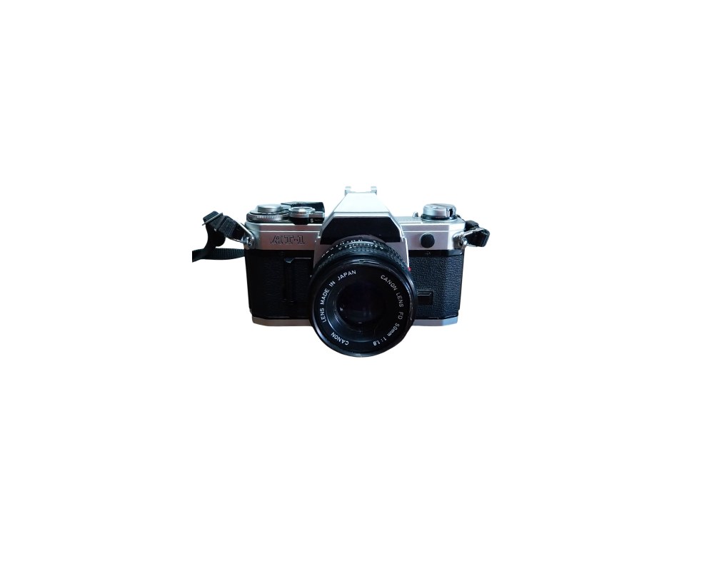 cámara fotográfica réflex analógica de época con un cuerpo metálico y revestimiento negro, correspondiente al emblemático modelo Canon AT-1, equipada con un objetivo Canon Lens FD de 50mm y una correa de transporte lateral alquiler oara eventos, publicidad, peliculas y series