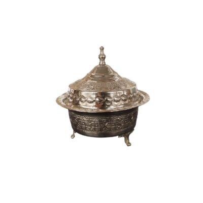 recipiente decorativo de época elaborado en metal con acabado plateado y patinado, caracterizado por su cuerpo semiesférico apoyado sobre pequeñas patas ornamentales, un borde de ala ancha y una elegante tapa cónica con remate superior y ricos grabados geométricos alquiler para eventos, publicidad, peliculas y series