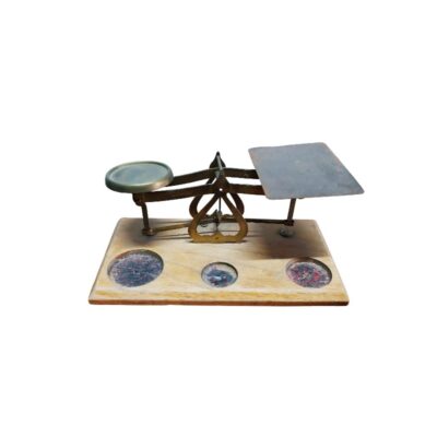 balanza de precisión de época con estructura de latón dorado, caracterizada por un sistema mecánico de balancín con dos platillos asimétricos (uno circular y otro rectangular) montados sobre una sólida base rectangular de madera que incorpora cavidades circulares con incrustaciones decorativas alquiler para eventos, publicidad, peliculas y series