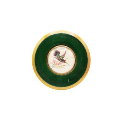 objeto decorativo circular de época, caracterizado por un diseño central de porcelana finamente pintado a mano que representa un colibrí entre flores, enmarcado por una amplia banda verde y un borde exterior de tonos claros alquiler para eventos, publicidad, peliculas y series