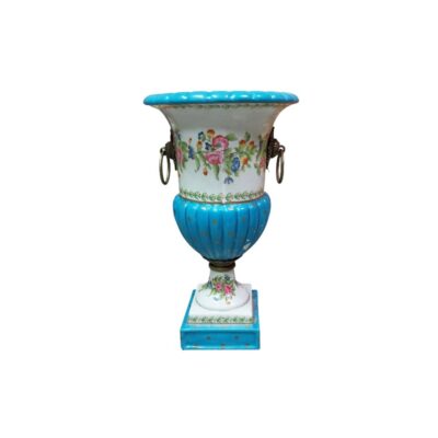 urna decorativa de época elaborado en porcelana fina, caracterizado por su cuerpo de diseño clásico con base cuadrada, peana y cuerpo acanalados en esmalte turquesa con lunares dorados, cuello ancho con delicadas guirnaldas y motivos florales policromados pintados a mano, y asas laterales metálicas en forma de anilla suspendida de mascarones alquiler para eventos, publicidad, peliculas y series