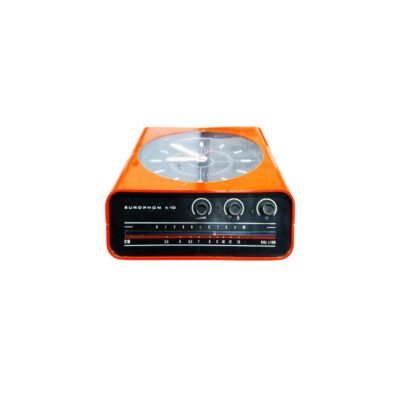 radio con reloj integrado de época de la marca Europhon (modelo h10), caracterizada por su llamativa carcasa de plástico en color naranja brillante de líneas aerodinámicas, con un reloj analógico superior de esfera oscura y un panel frontal inferior que integra los mandos de control y la franja del dial de sintonización alquiler para eventos, publicidad, peliculas y series