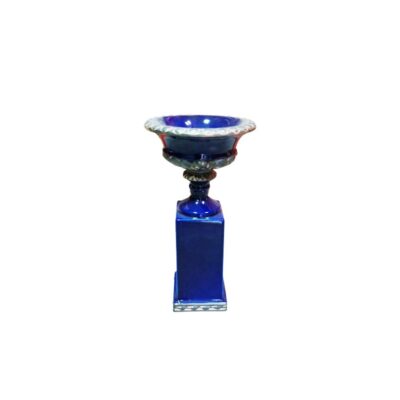 urna decorativa de época elaborada en cerámica esmaltada en un profundo tono azul añil, caracterizada por su copa superior moldurada con cenefas en relieve y un soporte elevado sobre una sólida base cuadrada alquiler para eventos, publicidad, peliculas y series