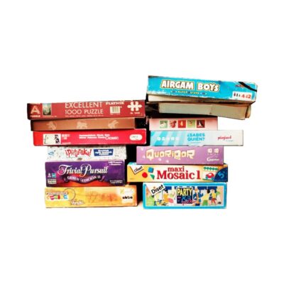 colección de juegos de mesa y cajas de juguetes de época, caracterizada por una amplia variedad de cajas apiladas de títulos clásicos como Trivial Pursuit, Airgamboys, Puzzles y juegos de salón, junto con un maletín de fiesta "Party Fun in a Box" con juguetes y accesorios variados alquiler para eventos, publicidad, peliculas y series